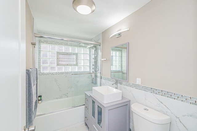 full bathroom with vanity, toilet, enclosed tub / shower combo, and tile walls