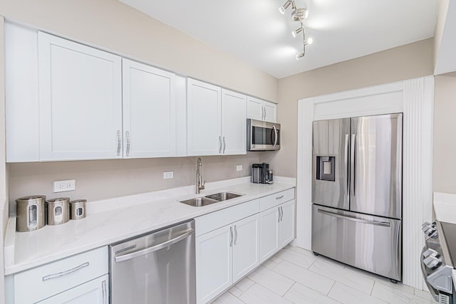 kitchen with light stone counters, stainless steel appliances, white cabinetry, and sink