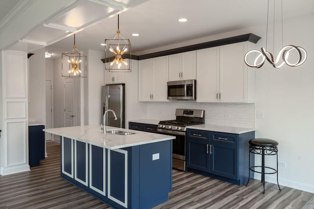 kitchen featuring stainless steel appliances, sink, blue cabinetry, decorative light fixtures, and an island with sink