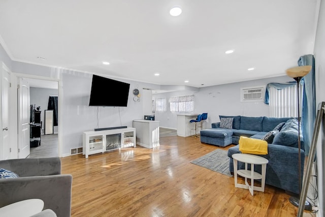 living room featuring hardwood / wood-style floors, an AC wall unit, and crown molding