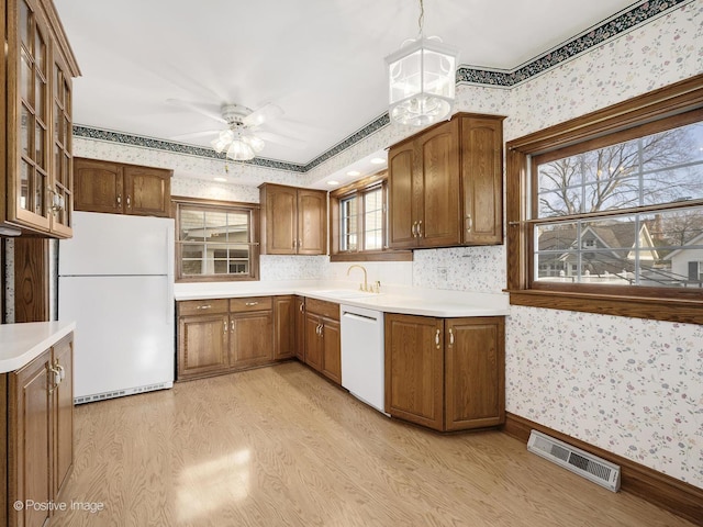 kitchen featuring light wood-type flooring, white appliances, ceiling fan, sink, and hanging light fixtures