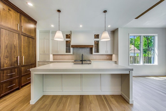 kitchen featuring backsplash, custom exhaust hood, a large island with sink, light hardwood / wood-style flooring, and white cabinetry