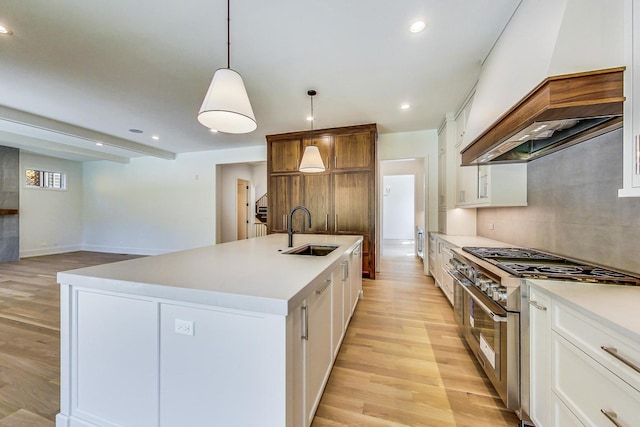 kitchen with a center island with sink, white cabinets, range with two ovens, and sink