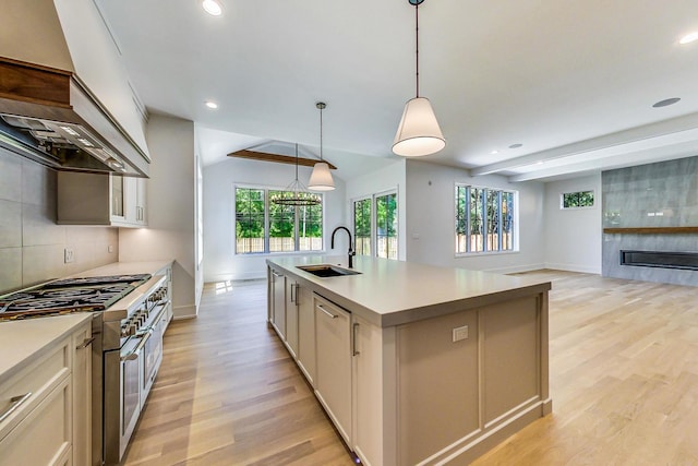 kitchen with backsplash, sink, a center island with sink, double oven range, and hanging light fixtures