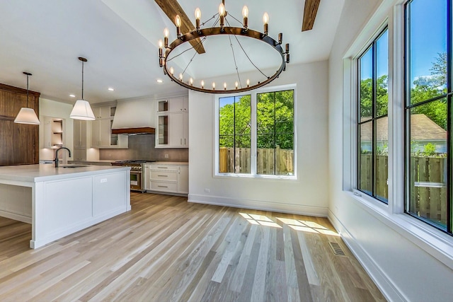 kitchen featuring hanging light fixtures, custom range hood, stainless steel range, a notable chandelier, and white cabinetry