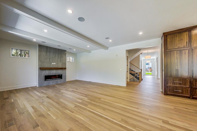 unfurnished living room with a fireplace, light hardwood / wood-style floors, and beamed ceiling