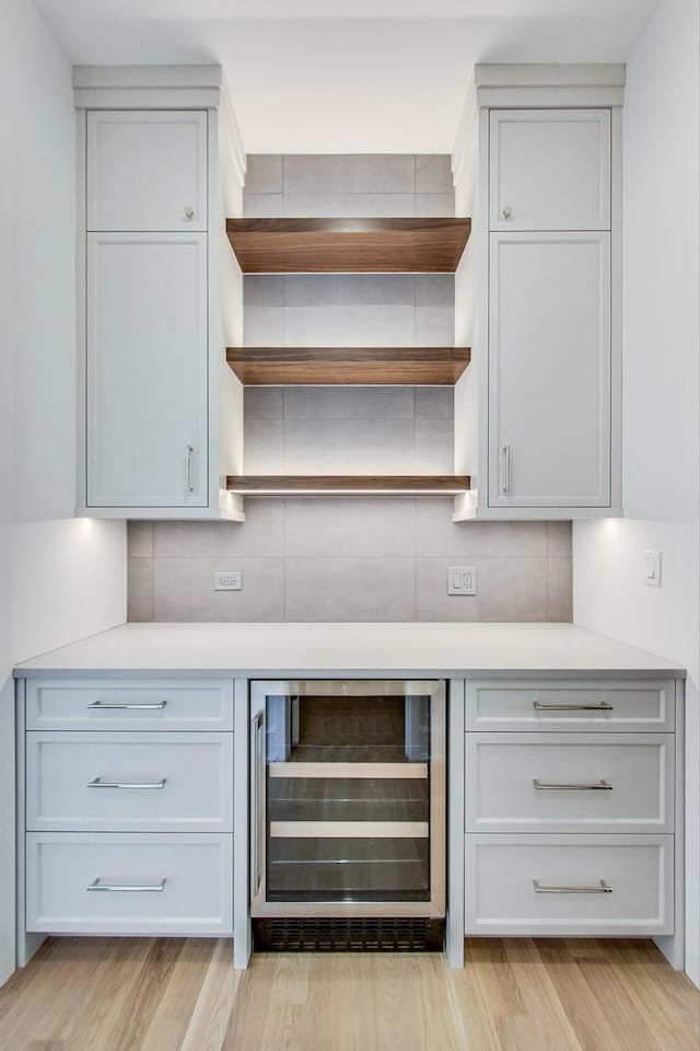 bar featuring white cabinets, light wood-type flooring, wine cooler, and backsplash