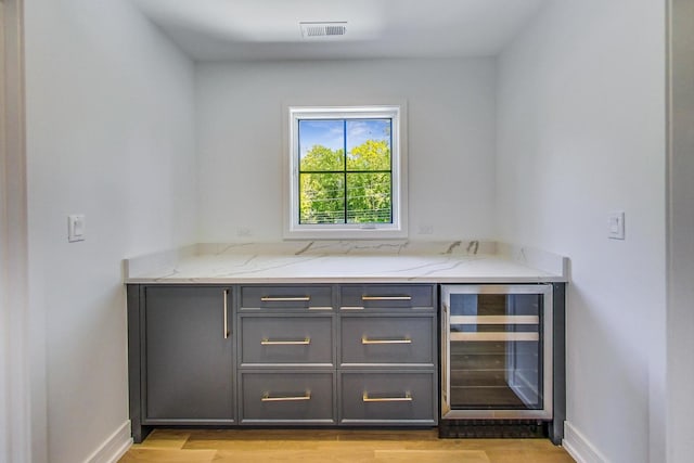 bar with light stone countertops, light hardwood / wood-style floors, wine cooler, and gray cabinetry