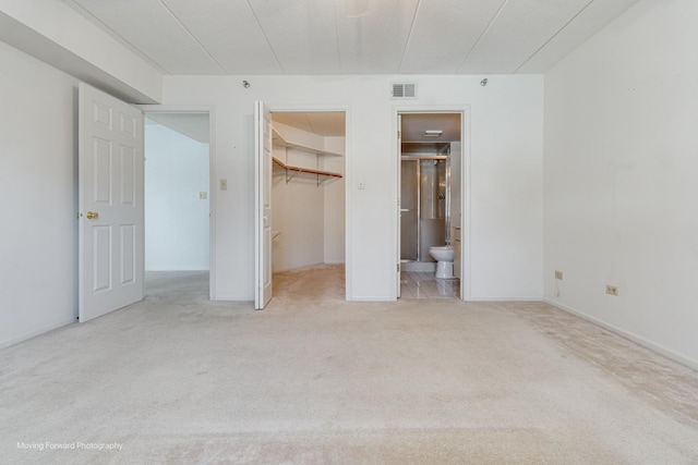 unfurnished bedroom featuring connected bathroom, a spacious closet, a closet, and light carpet