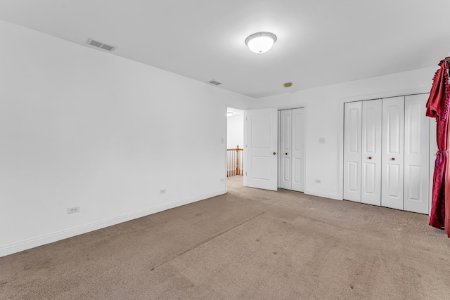 unfurnished bedroom with light colored carpet and multiple closets