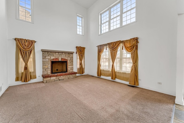 unfurnished living room with a stone fireplace, carpet floors, and a towering ceiling