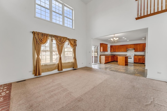 unfurnished living room with a towering ceiling, light colored carpet, and a notable chandelier