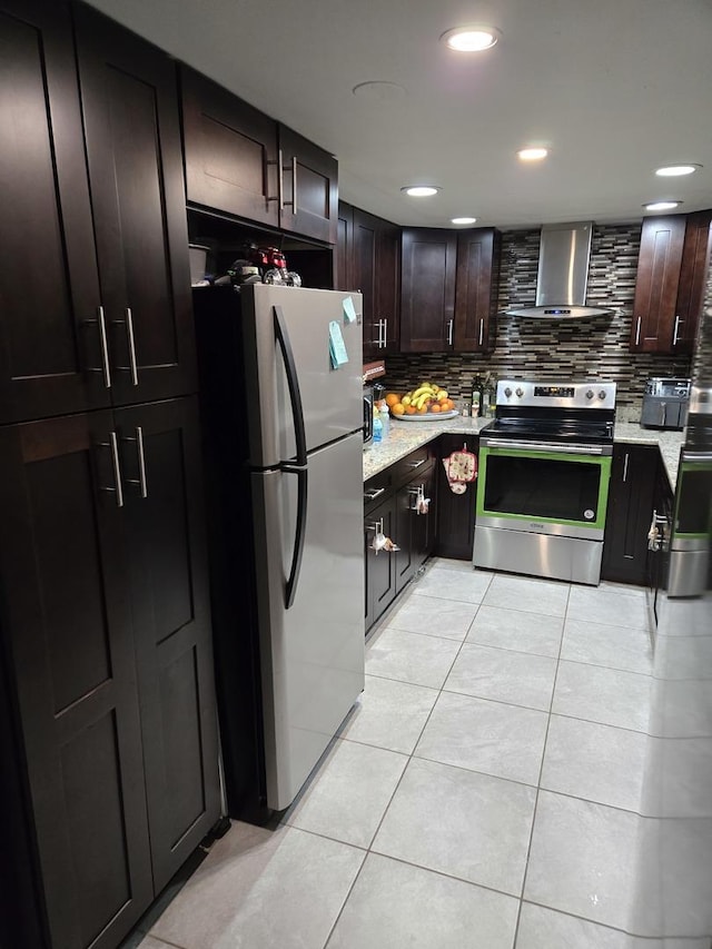 kitchen featuring wall chimney exhaust hood, stainless steel appliances, backsplash, dark brown cabinets, and light tile patterned flooring