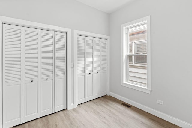 unfurnished bedroom with multiple closets and light wood-type flooring