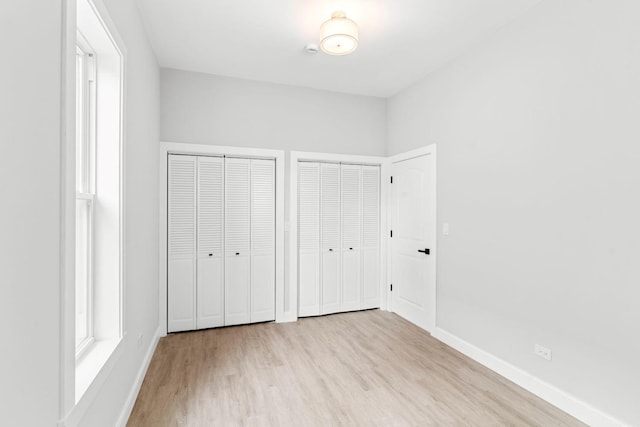 unfurnished bedroom featuring light wood-type flooring and two closets