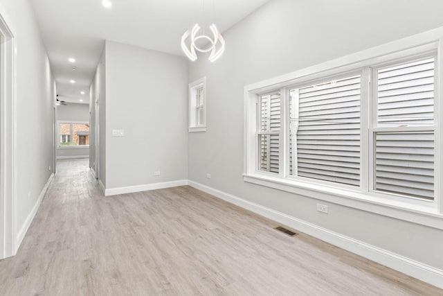 empty room featuring ceiling fan with notable chandelier and light wood-type flooring