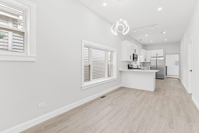 kitchen with white cabinets, rail lighting, decorative light fixtures, kitchen peninsula, and stainless steel refrigerator