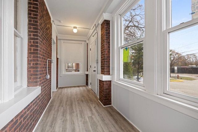 corridor featuring light wood-type flooring, ornamental molding, and brick wall