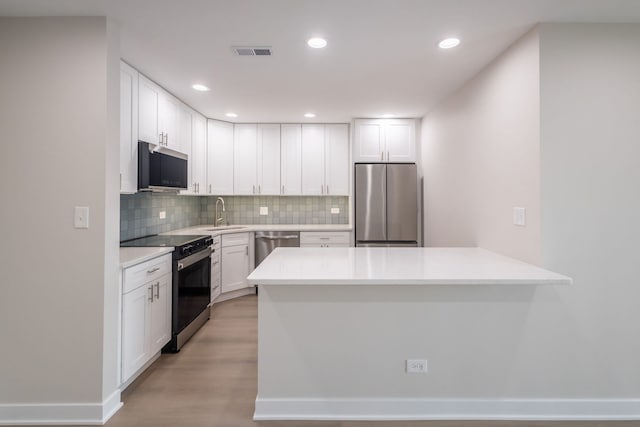 kitchen with kitchen peninsula, appliances with stainless steel finishes, backsplash, white cabinets, and light hardwood / wood-style flooring