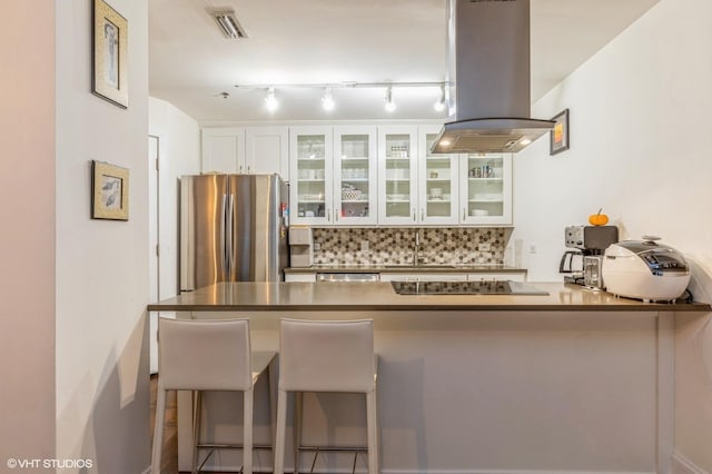 kitchen featuring decorative backsplash, kitchen peninsula, island range hood, white cabinets, and appliances with stainless steel finishes