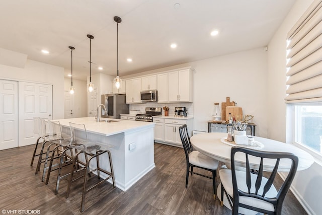 kitchen with decorative backsplash, appliances with stainless steel finishes, decorative light fixtures, white cabinets, and an island with sink