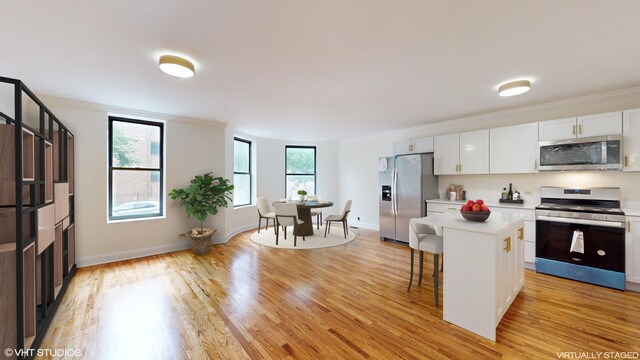 kitchen with light wood-type flooring, a breakfast bar, stainless steel appliances, white cabinets, and a center island