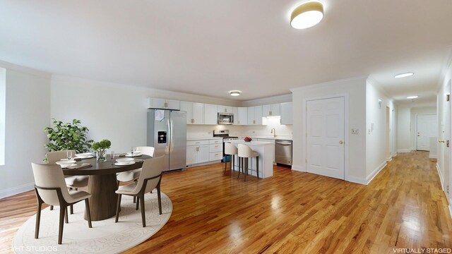 kitchen with white cabinetry, a kitchen breakfast bar, appliances with stainless steel finishes, a kitchen island, and light wood-type flooring