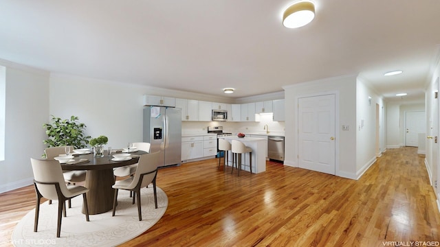 dining space featuring ornamental molding, sink, and light hardwood / wood-style flooring