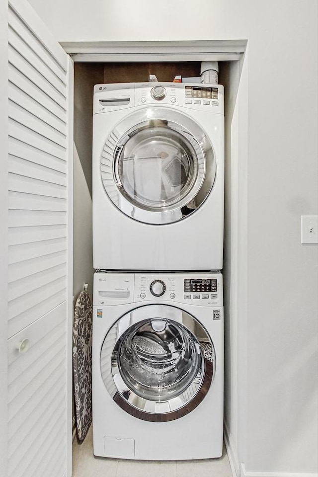 laundry room featuring stacked washing maching and dryer and light tile patterned floors