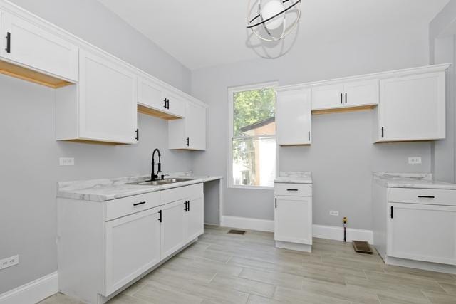 kitchen featuring light stone counters, sink, white cabinets, and pendant lighting