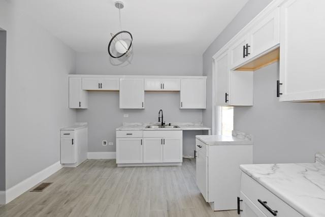 kitchen featuring white cabinetry, sink, light stone counters, light hardwood / wood-style floors, and decorative light fixtures