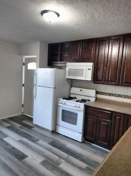 kitchen featuring a textured ceiling, white appliances, dark hardwood / wood-style flooring, and dark brown cabinetry