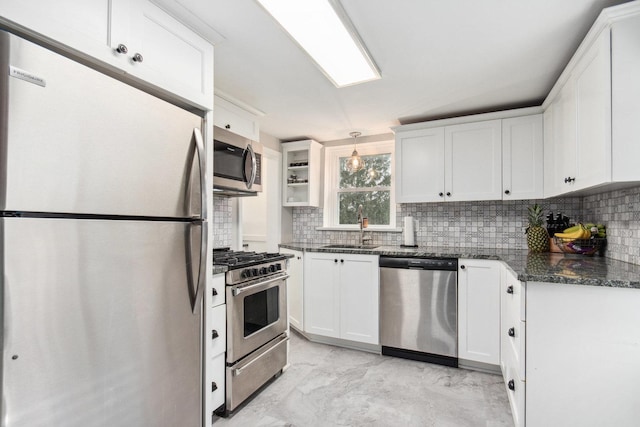 kitchen featuring dark stone counters, stainless steel appliances, sink, pendant lighting, and white cabinets