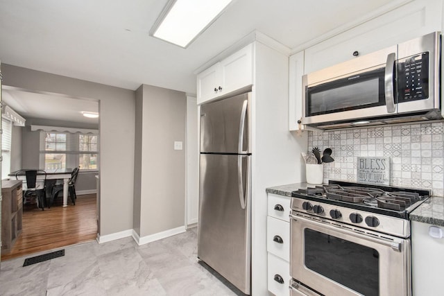 kitchen featuring tasteful backsplash, dark stone countertops, white cabinets, and stainless steel appliances