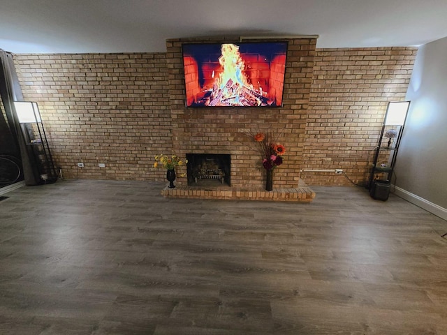 unfurnished living room with hardwood / wood-style flooring, brick wall, and a fireplace