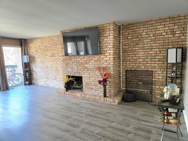 unfurnished living room with a brick fireplace, brick wall, and wood-type flooring