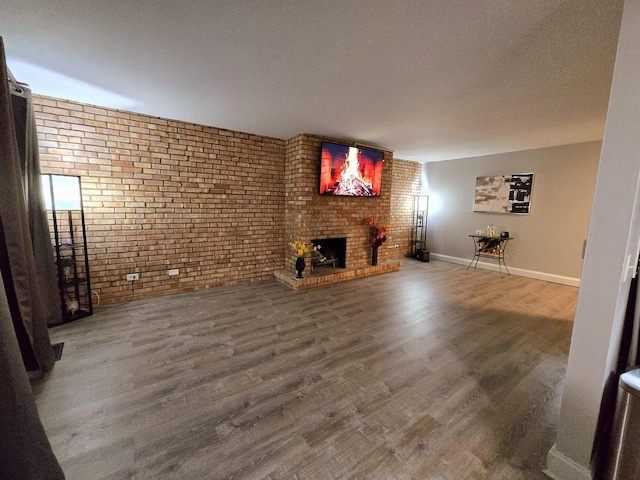 unfurnished living room with a brick fireplace, brick wall, a textured ceiling, and hardwood / wood-style floors