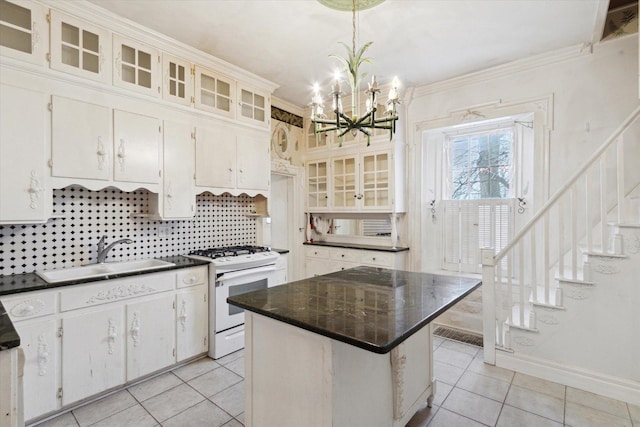 kitchen featuring white gas range, sink, hanging light fixtures, a kitchen island, and white cabinets