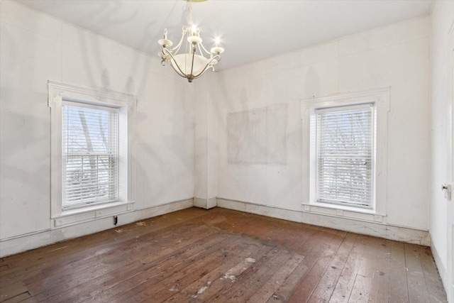 spare room with a wealth of natural light, dark hardwood / wood-style flooring, and a chandelier