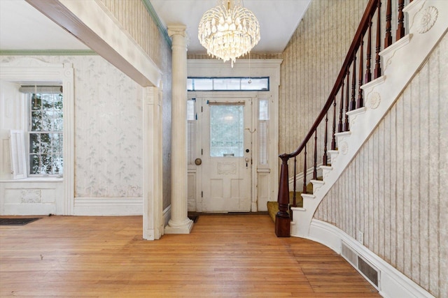 foyer entrance featuring ornate columns, crown molding, wood-type flooring, and an inviting chandelier