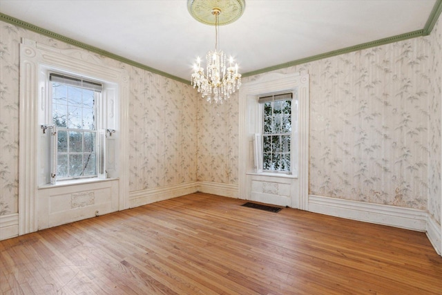 unfurnished dining area featuring hardwood / wood-style floors, crown molding, and a notable chandelier