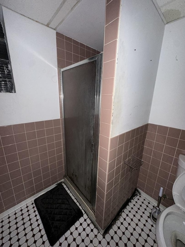 bathroom featuring an enclosed shower, toilet, and tile walls