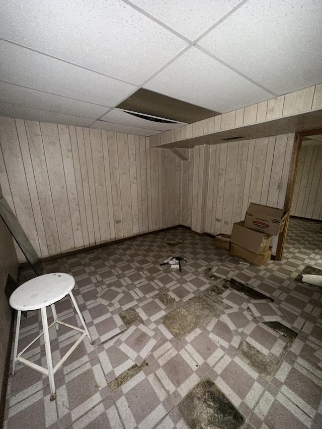 basement featuring a paneled ceiling and wooden walls