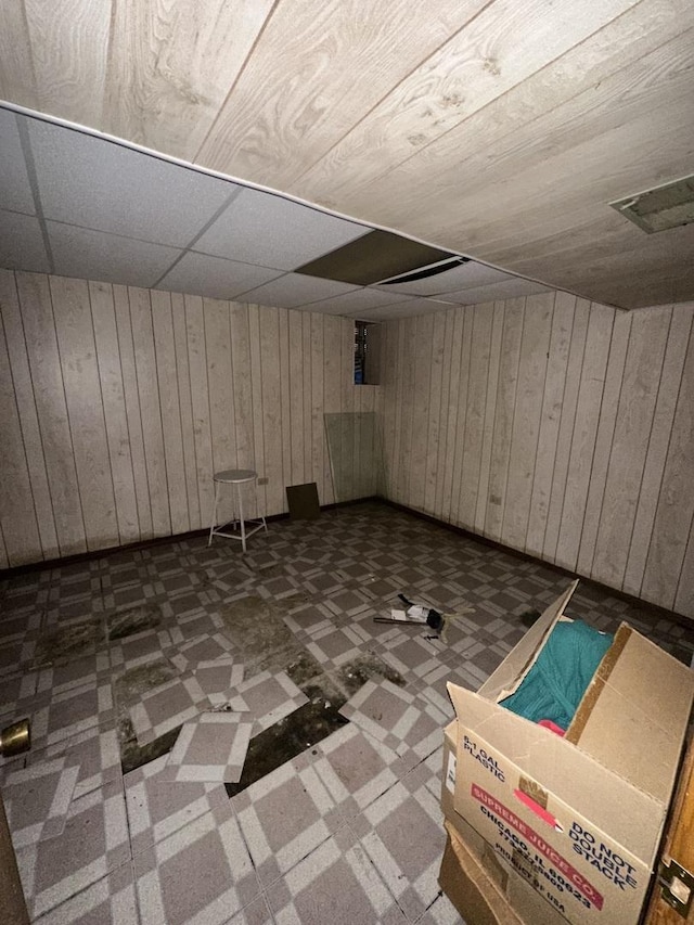 basement with a paneled ceiling and wood walls