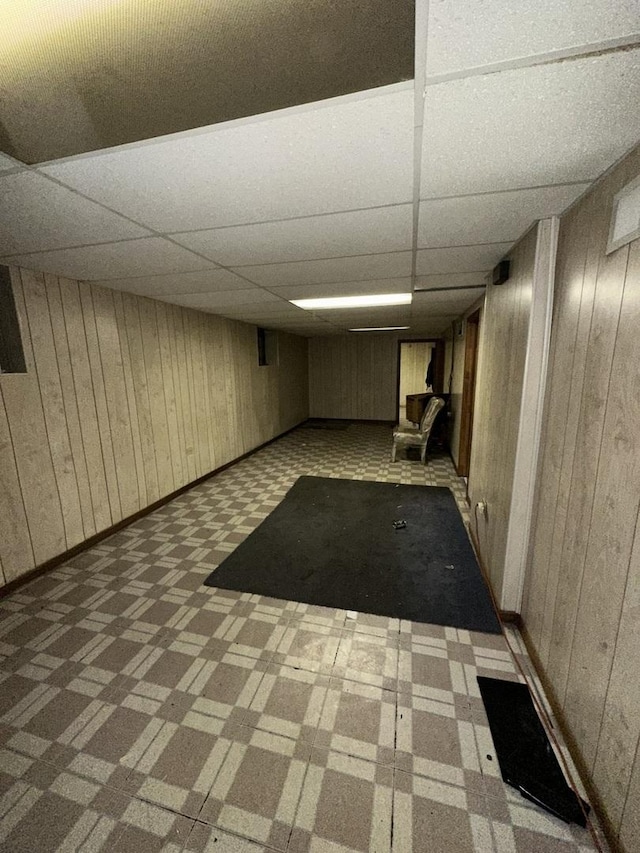 basement featuring a paneled ceiling and wood walls