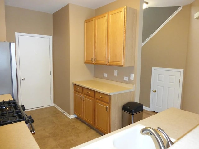 kitchen featuring black gas range, light brown cabinets, and stainless steel refrigerator