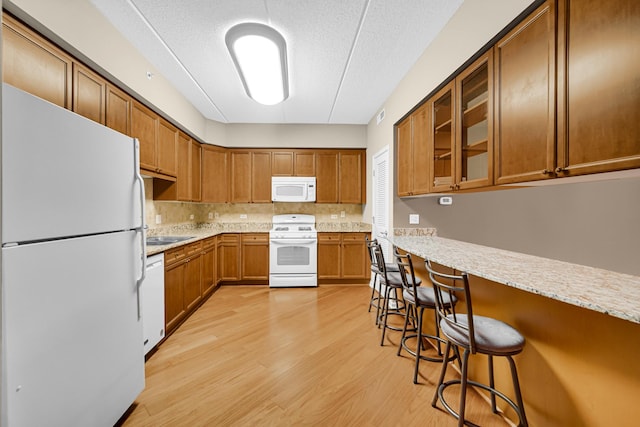 kitchen with white appliances, a kitchen breakfast bar, light stone countertops, a textured ceiling, and light hardwood / wood-style floors