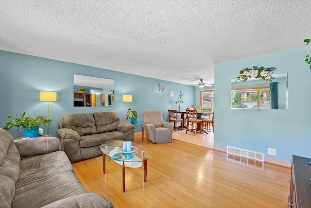 living room featuring hardwood / wood-style flooring, ceiling fan, and a textured ceiling