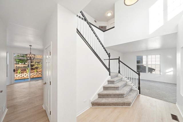 staircase featuring wood-type flooring, a towering ceiling, and a healthy amount of sunlight