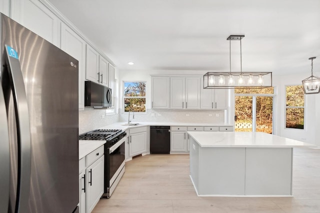 kitchen featuring hanging light fixtures, plenty of natural light, a kitchen island, white cabinetry, and stainless steel appliances